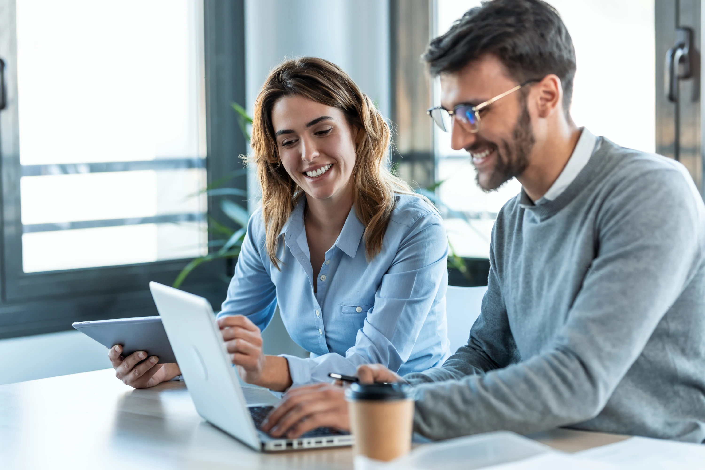 Two office workers looking over a laptop at desk